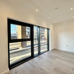 Empty room with large window and light wood flooring.
