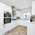 Modern white kitchen with integrated appliances and wood floor.