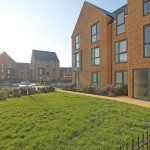 Modern brick apartment buildings with sunny lawn.
