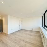 Empty modern apartment with large windows and kitchenette.