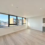 Modern empty flat with large windows and kitchen area.