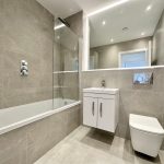 Modern grey tiled bathroom with bathtub and mirror.