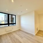 Bright, modern flat with large window and light flooring.