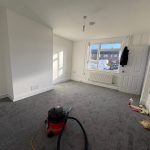 Empty room with grey carpet and vacuum cleaner.