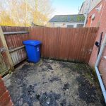 Outdoor area with blue wheelie bin and wooden fence.