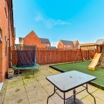 Garden with trampoline, playhouse, slide, and patio.