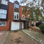 Brick townhouse with driveway and garage, trees nearby.