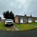 White car parked outside brick bungalow.