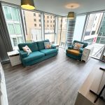 Modern living room with large windows and teal furniture.