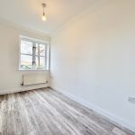 Minimalist empty room with wooden flooring and window.