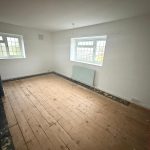Empty room with wooden floorboards and windows.
