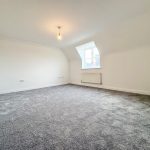 Spacious empty room with grey carpet and window.