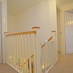 Bright corridor with white doors and stair railing.