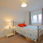 Cosy bedroom with floral bedspread and bedside lamp.