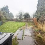 Overgrown garden with bins and stone walls.