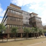 Modern office building with glass facade and trees.