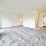 Spacious carpeted room with white walls and doorway.