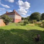Semi-detached house with spacious green garden under blue sky.