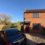 Brick house with car in driveway, sunny day.