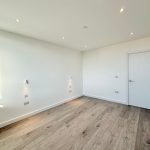 Minimalist empty room with wooden flooring and spotlights.