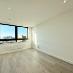 Empty bright room with large window and wooden floor.