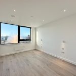 Bright, empty room with large window and wood floor.