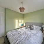 Bedroom with light green walls and grey bed.