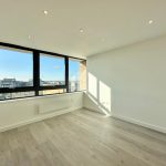 Bright empty room with large window and wooden floor.