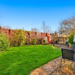 Sunny garden with lawn and patio chairs.