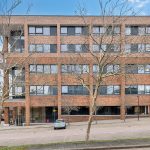 Four-storey brick building with large windows and trees.