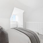 Bright bedroom with grey bedding and window view.