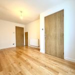 Empty room with wooden flooring and closed doors.