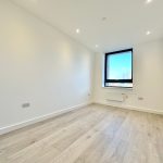 Empty modern room with large window and wooden floor.