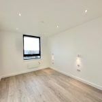 Spacious empty room with large window and wooden floor.