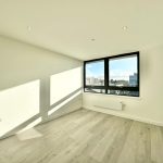 Bright empty room with large window and wooden floor.