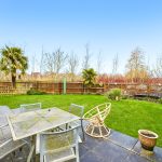 Back garden with patio and lawn on sunny day.