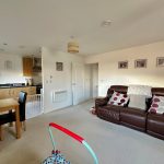 Spacious living room with kitchen and brown sofa.