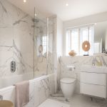Modern bathroom with marble tiles and white fixtures.
