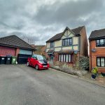 Red car in driveway of suburban house.