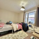 Messy bedroom with bed, suitcase, and window view.