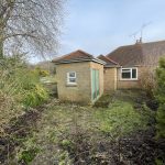 Backyard of a brick house with overgrown garden.