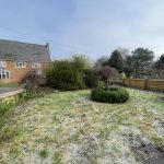 Frosty garden with house and trees in background.
