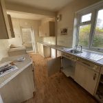 Empty, worn kitchen with open cupboards and window view.