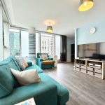 Modern living room with teal sofas and large TV.