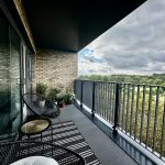 Modern balcony with chairs overlooking green landscape.