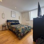 Modern bedroom with floral bedding and wooden flooring.