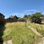 Overgrown garden with stone house and blue sky.
