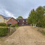 Large countryside house with gravel driveway and trees.