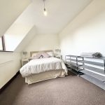 Spacious bedroom with bed and shelves, bright window view.