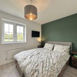 Modern bedroom with green accent wall and window view.